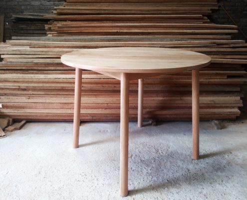 Pale wooden round table with round section legs that are slightly splayed out